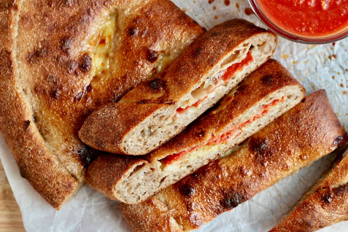 Pieces of sourdough calzone on a sheet of parchment paper next to a small bowl of marinara dipping sauce.