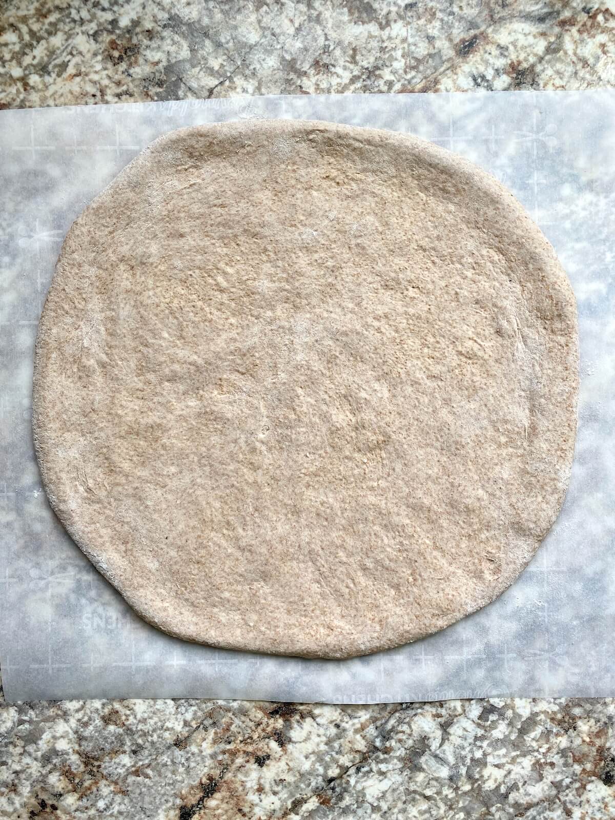 A sourdough pizza dough stretched out on a piece of parchment paper.