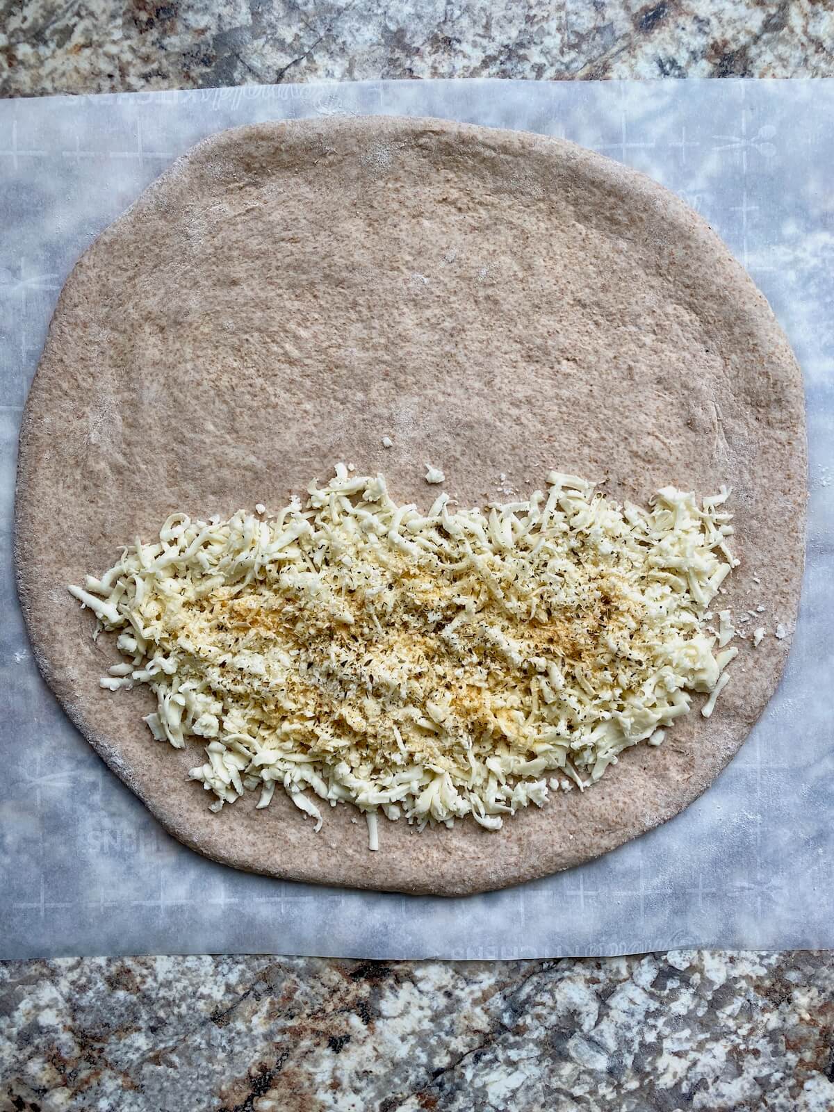 Mozzarella cheese, parmesan cheese, and seasonings on half of a stretched out sourdough pizza dough.
