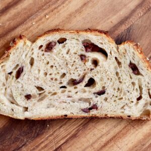 A slice of sourdough olive bread on a wooden cutting board.