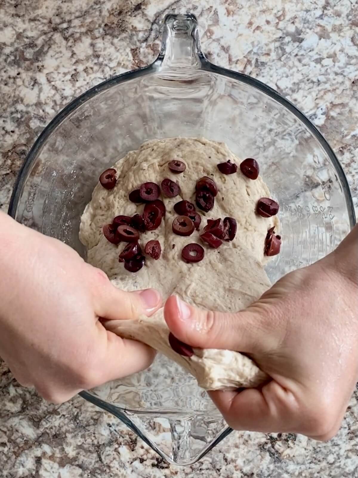 The sliced kalamata olives being stretched and folded into the dough.