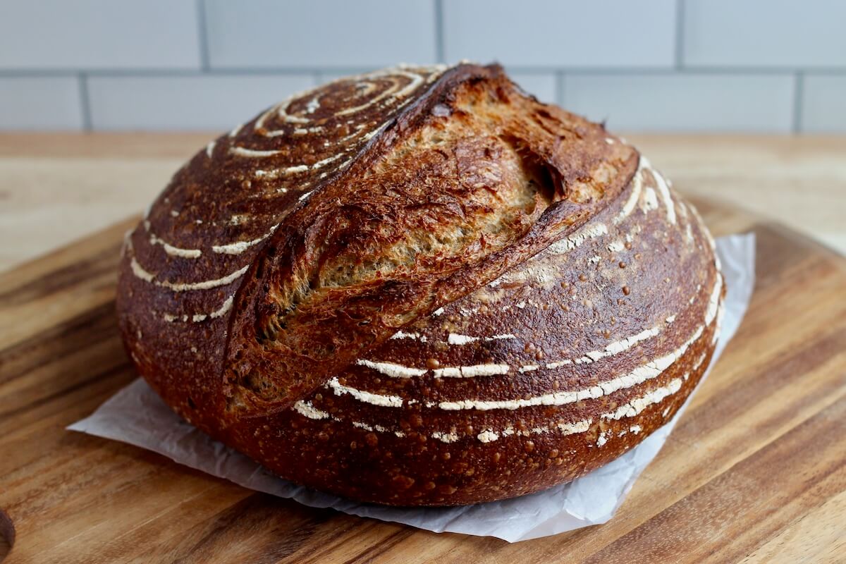 A whole loaf of sourdough rye bread on a wooden cutting board.