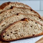 A loaf of sourdough rye bread cut into slices on a wooden cutting board.