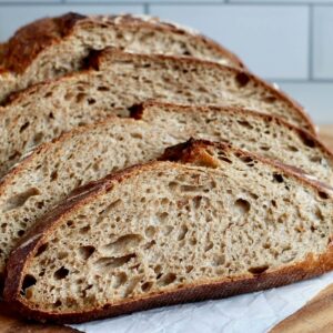 A loaf of sourdough rye bread cut into slices on a wooden cutting board.