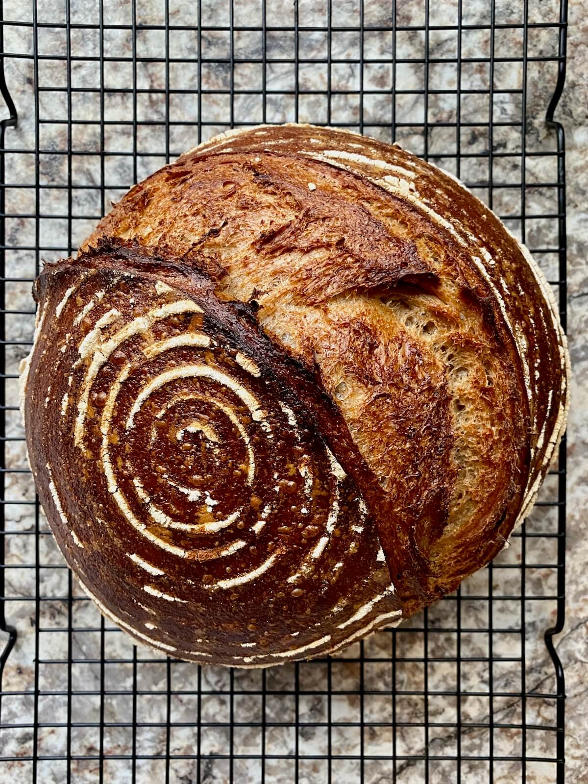A baked loaf of sourdough rye bread on a wire cooling rack.