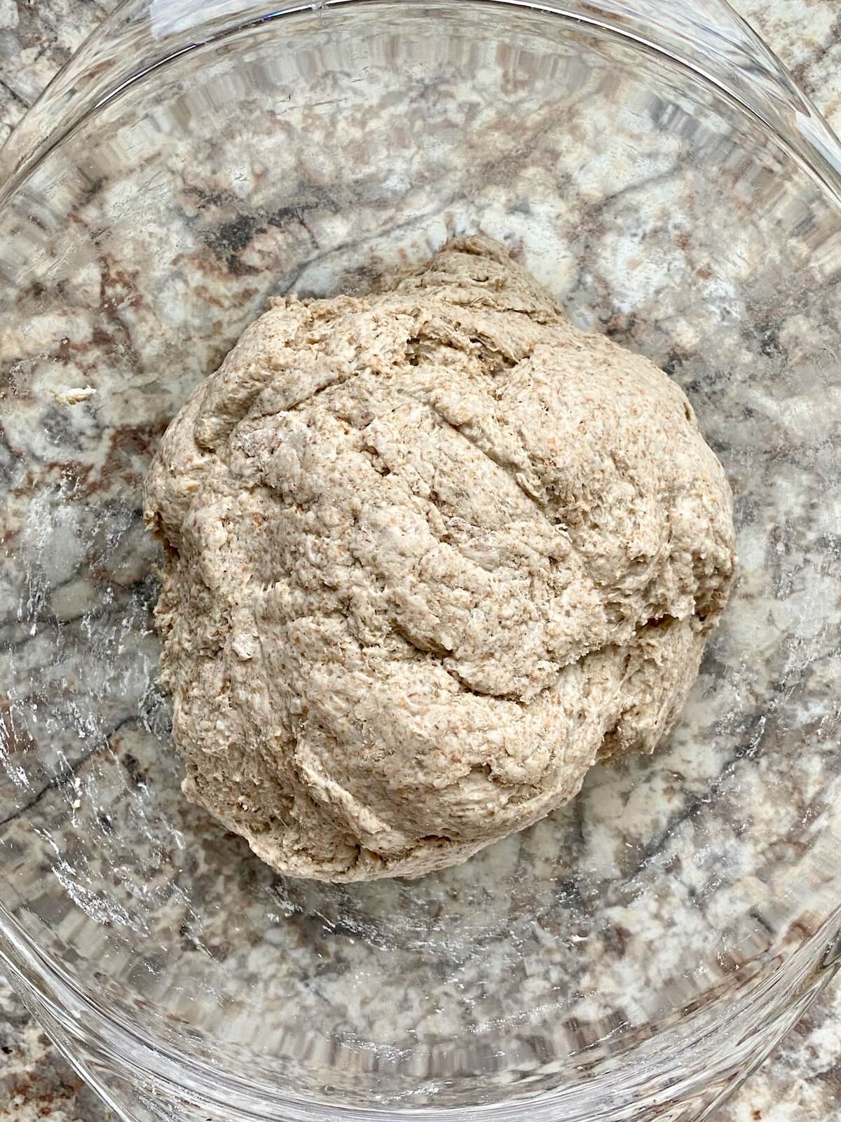 Bread flour, rye flour, and whole wheat flour mixed together with water in a glass bowl.