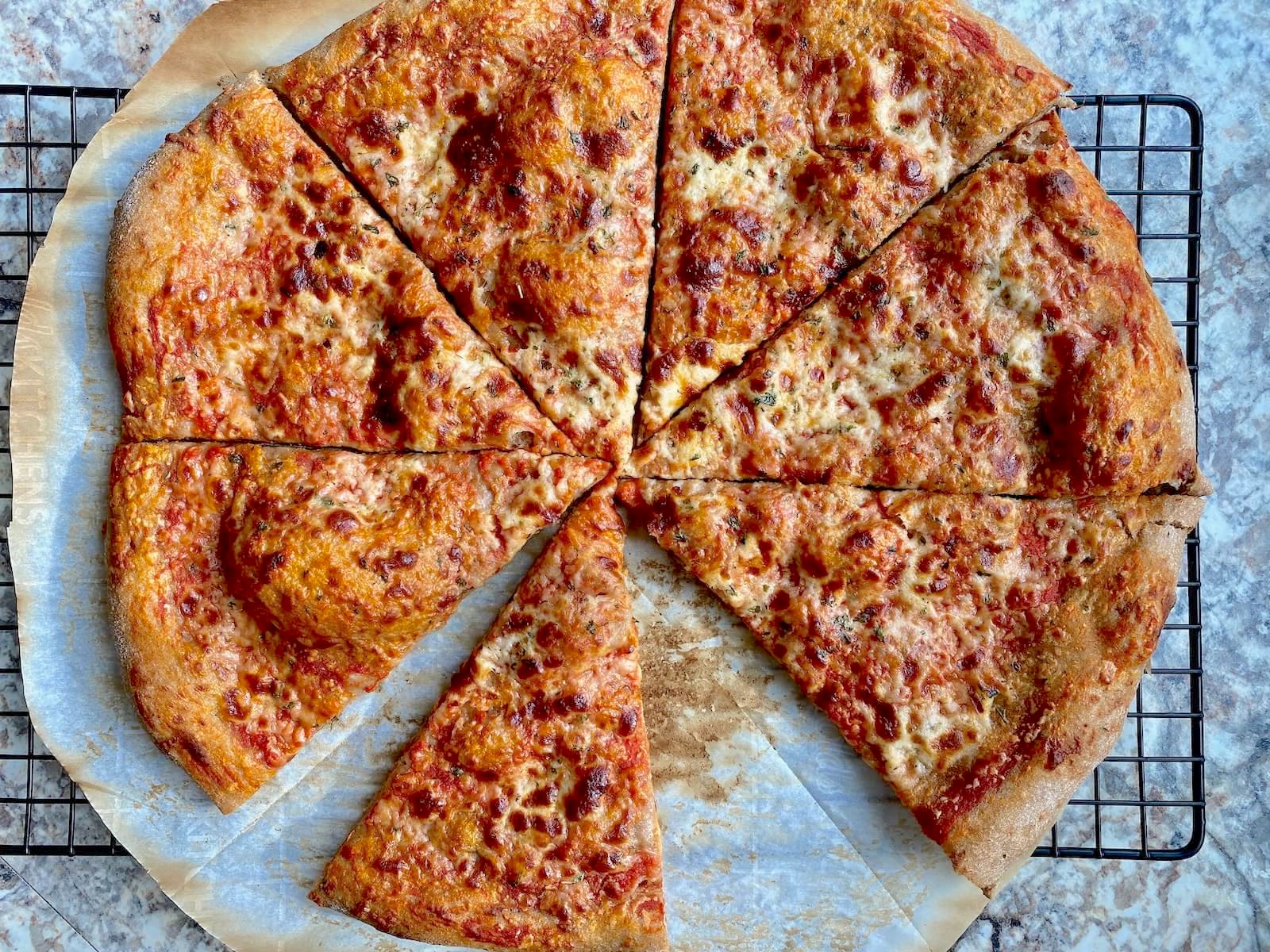 A cheese pizza made with whole wheat sourdough pizza dough cut into 8 slices on a wire cooling rack. One slice is missing from the pizza.