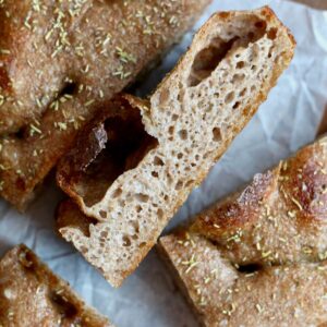 Several pieces of whole wheat sourdough focaccia on a piece of wrinkled parchment paper.