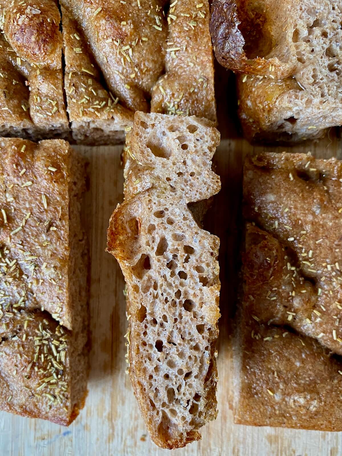 Sliced whole wheat sourdough focaccia on a cutting board. One piece of flipped over to show the crumb.