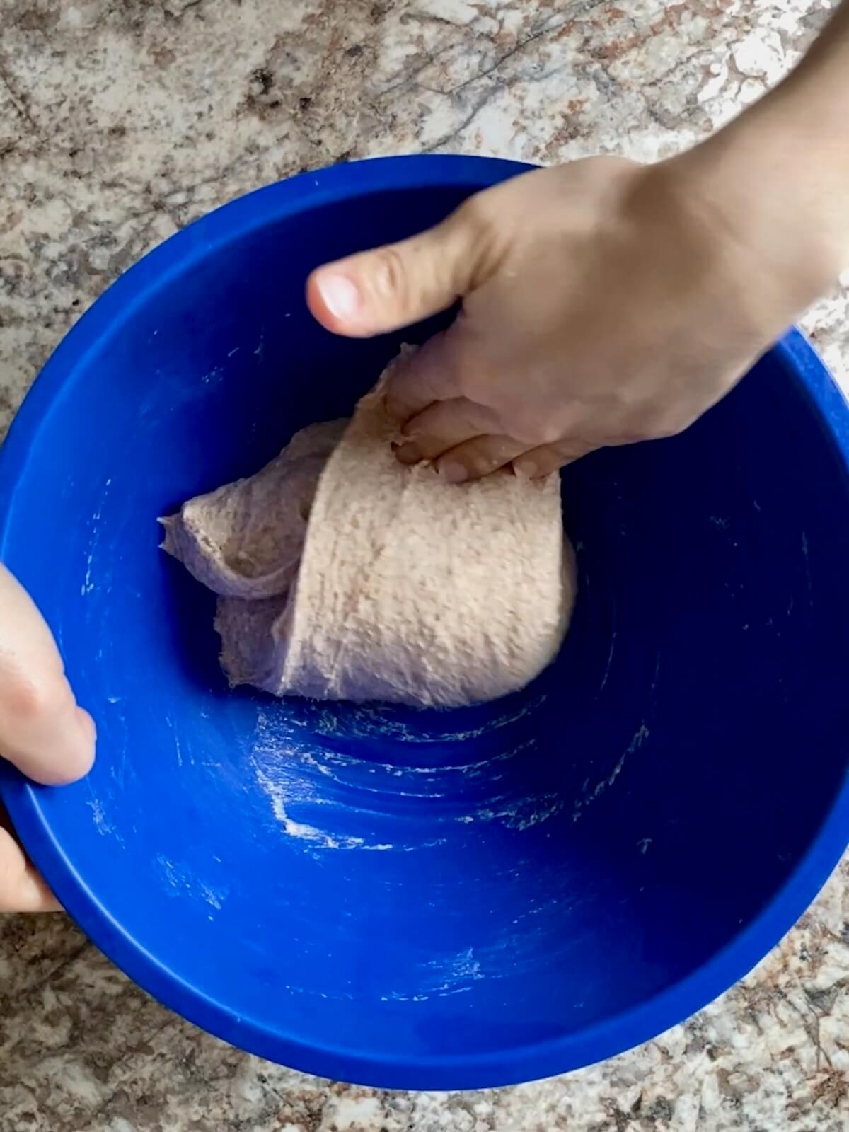The focaccia dough being stretched and folded in a bowl.