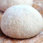 A sourdough whole wheat pizza dough ball on a floured pizza peel.
