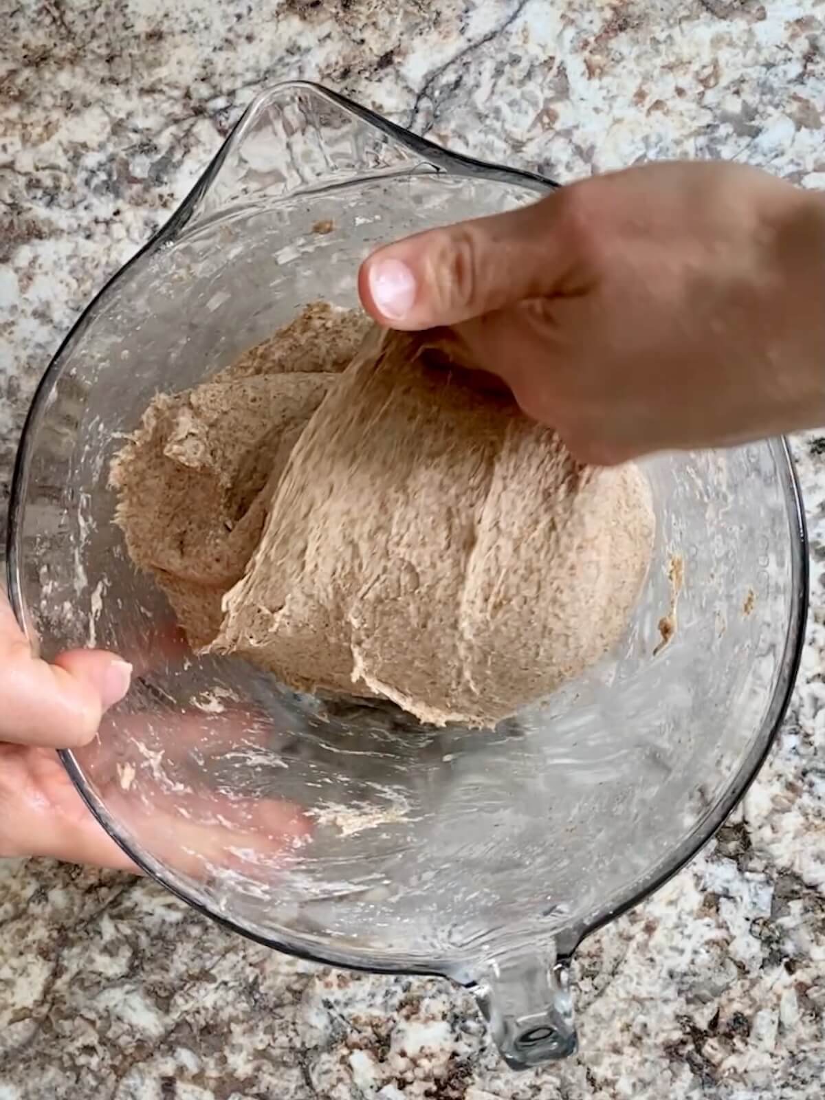 The dough being stretched and folded in a glass bowl.