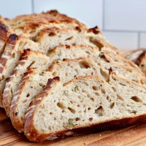 A loaf of dill pickle sourdough bread cut into slices on a wooden cutting board.