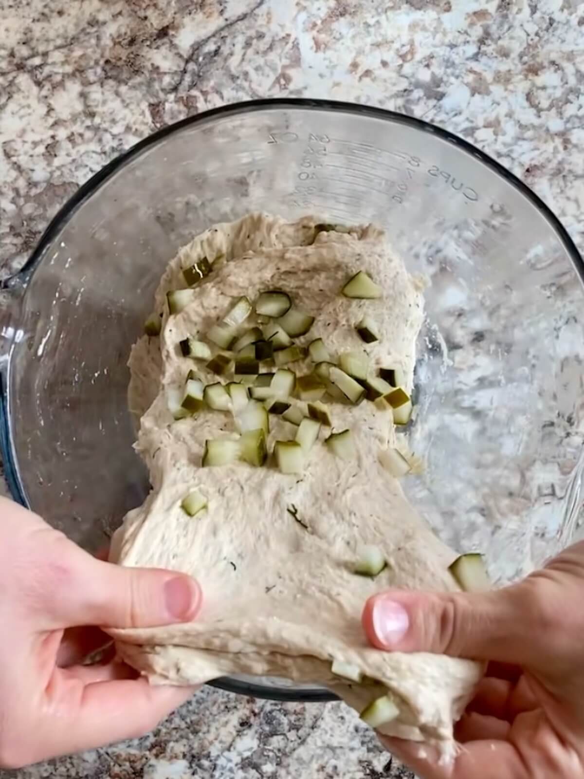 The dough being stretched and folded in a glass mixing bowl.