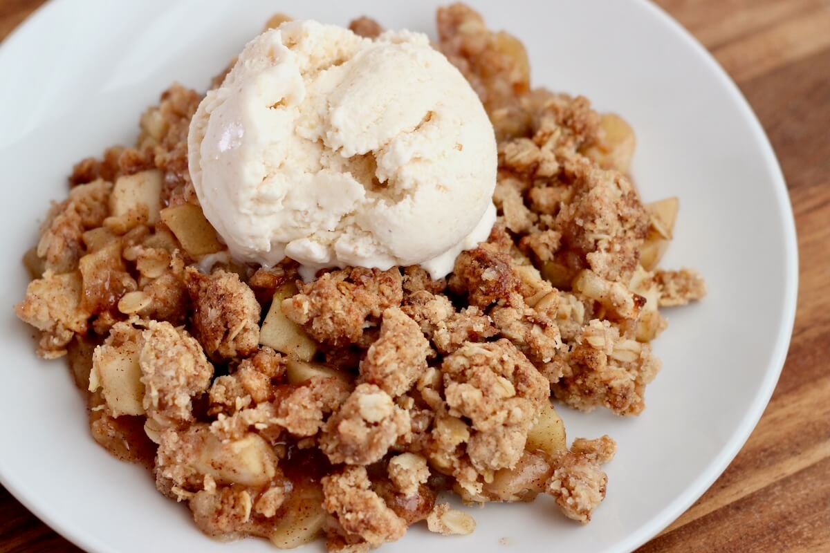 Sourdough apple crisp topped with ice cream on a small white plate.
