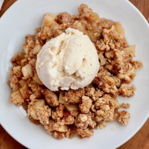 A small white plate of sourdough apple crisp topped with ice cream.