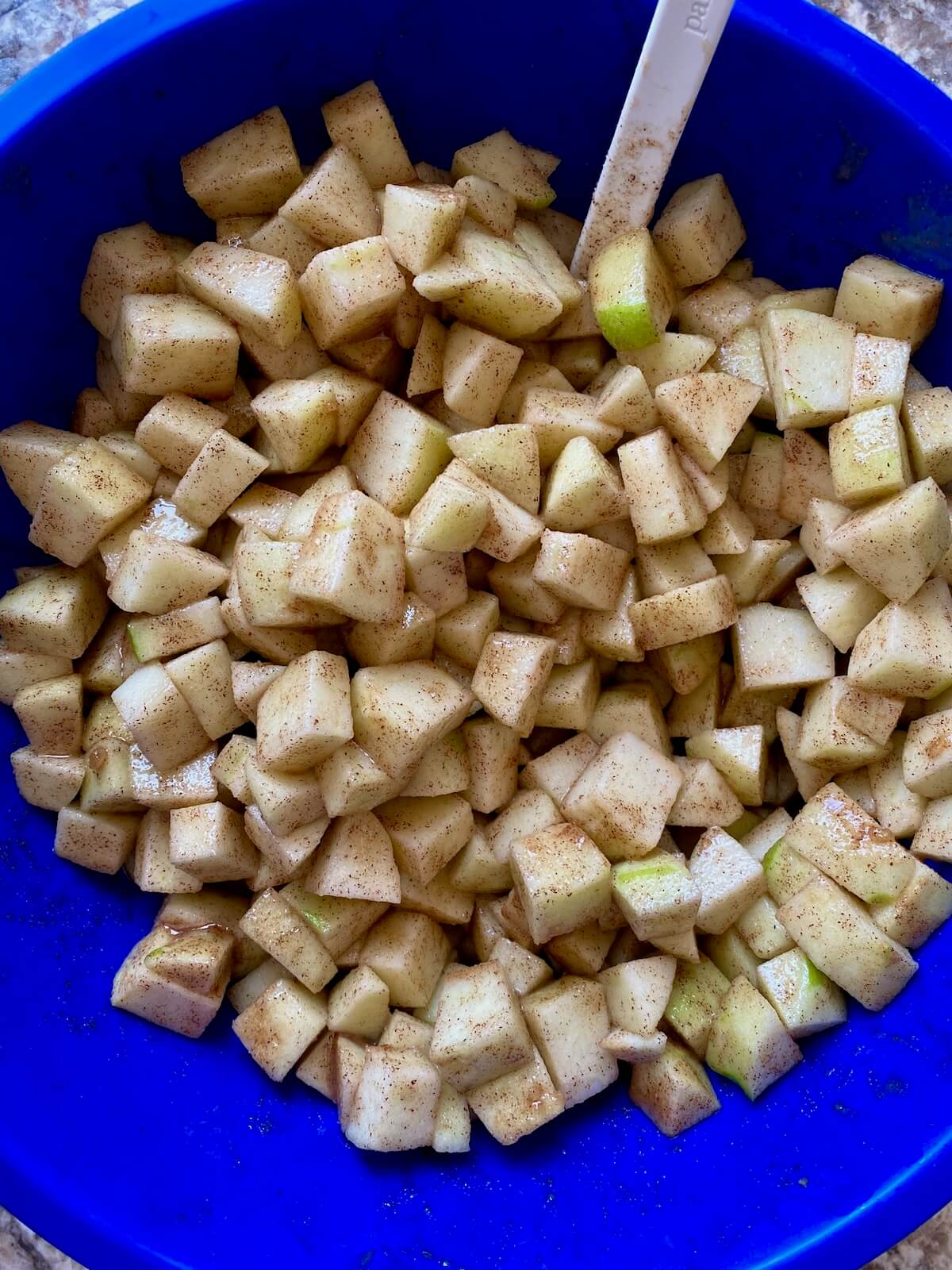 Diced apples mixed with cinnamon, sugar, and lemon juice in a blue mixing bowl.