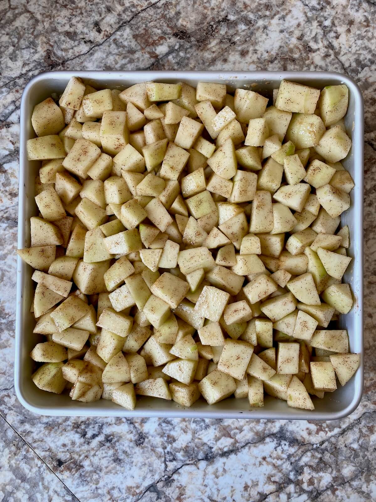 Diced apple filling in an 8-inch square aluminum baking pan.