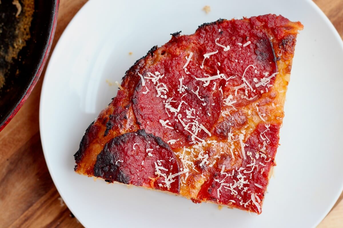 A piece of pepperoni sourdough pan pizza sprinkled with parmesan cheese on a small white plate.