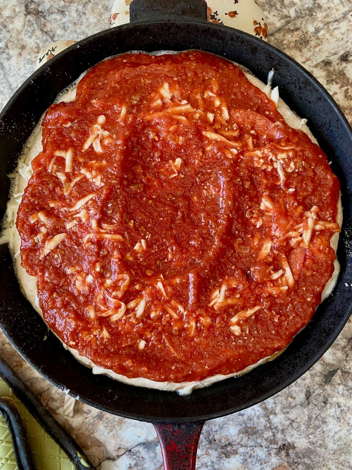 The pan pizza fully assembled in a hot cast iron skillet before baking.