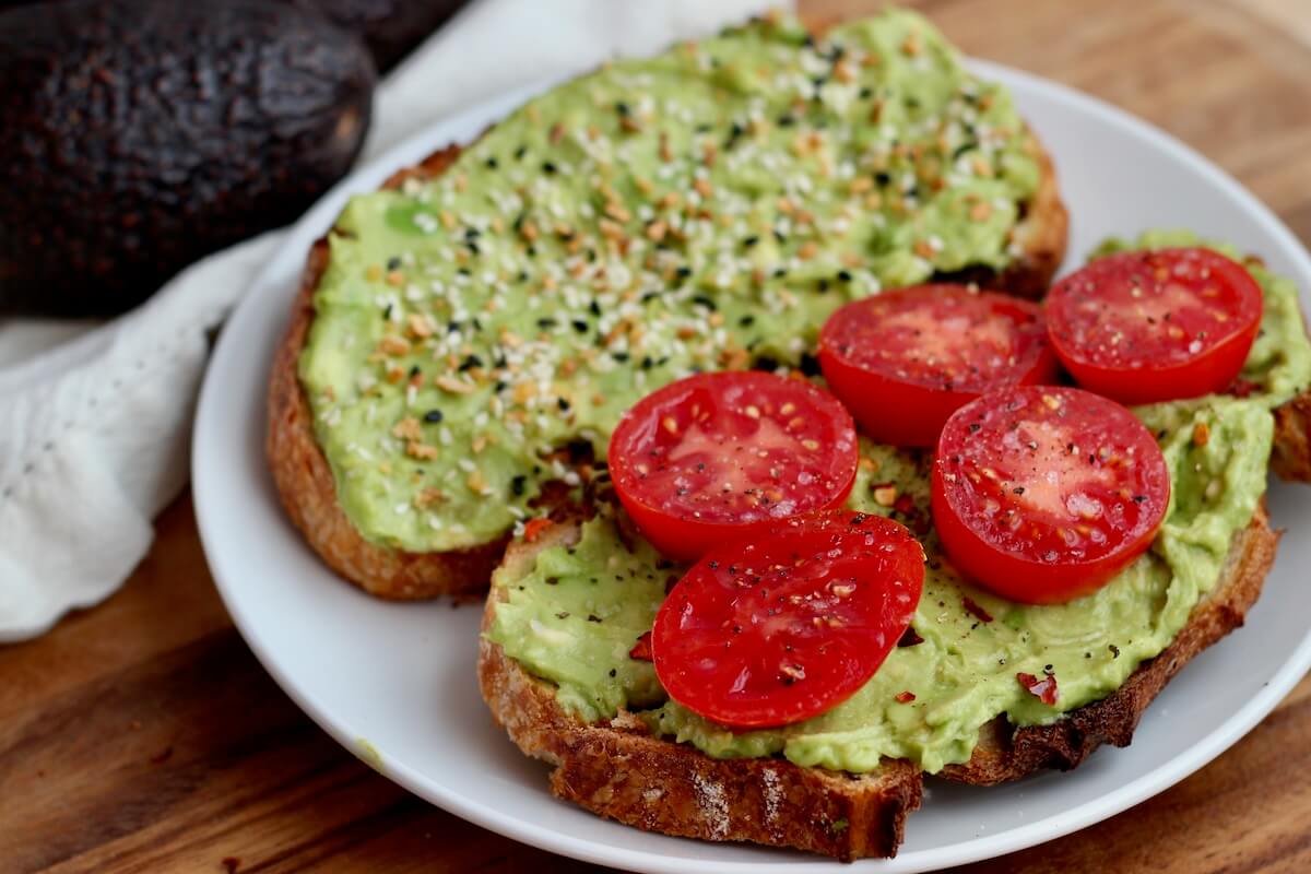 A plate with two pieces of avocado sourdough toast with toppings.
