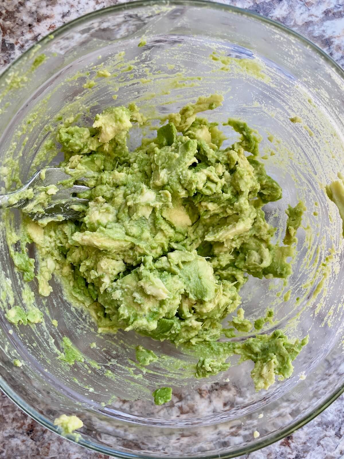 Avocado mashed with salt in a glass bowl.