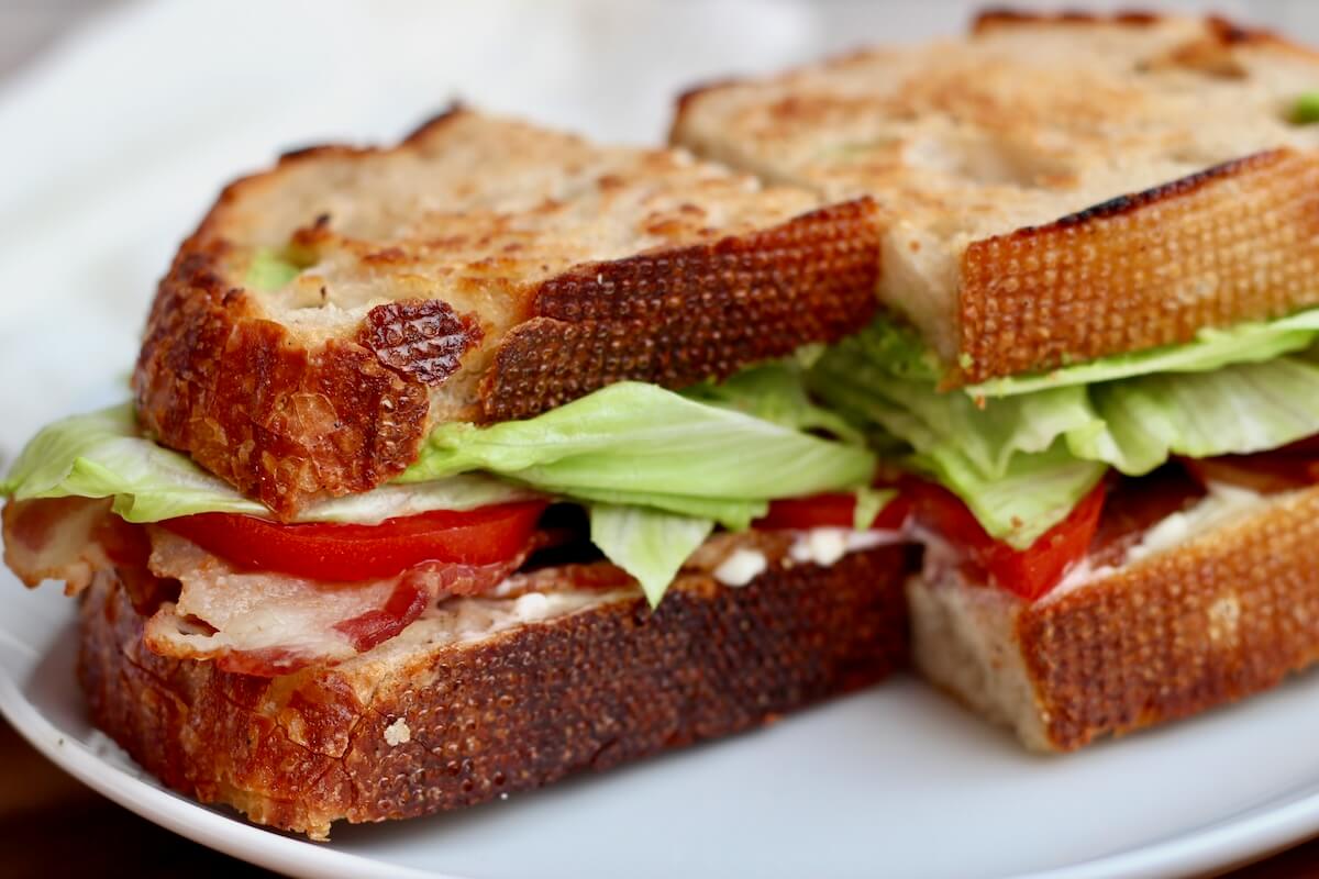 A sourdough BLT sandwich cut in half on a plate.