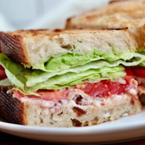 A BLT sandwich on sourdough bread cut in half on a plate.