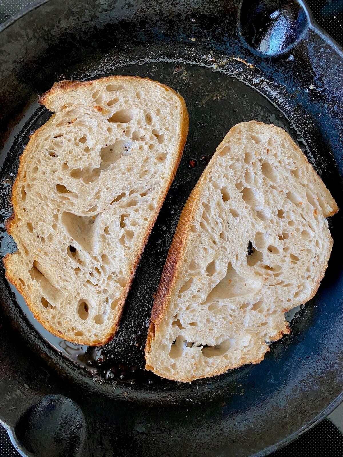Two slices of sourdough bread toasting in bacon fat in a cast iron skillet.