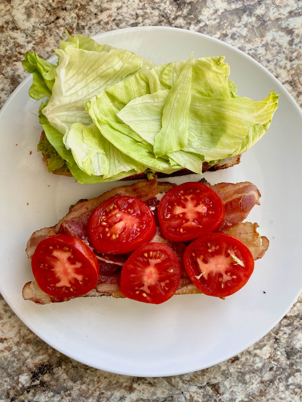 Bacon, sliced tomato, and iceberg lettuce on top of slices of sourdough bread.