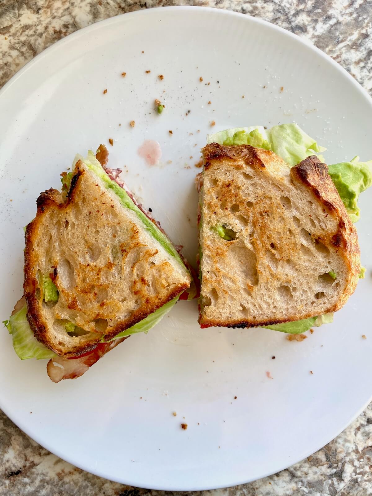 The assembled BLT sourdough sandwich cut in half on a small white plate.