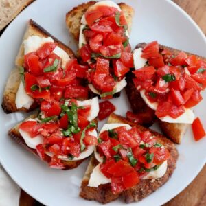 A small white plate with five pieces of sourdough bruschetta on it.
