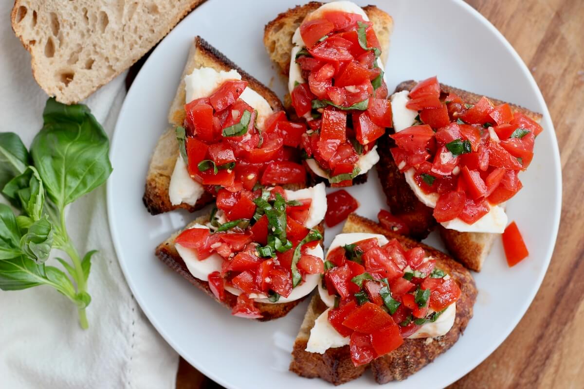 A small white plate with five pieces of sourdough bruschetta on it.
