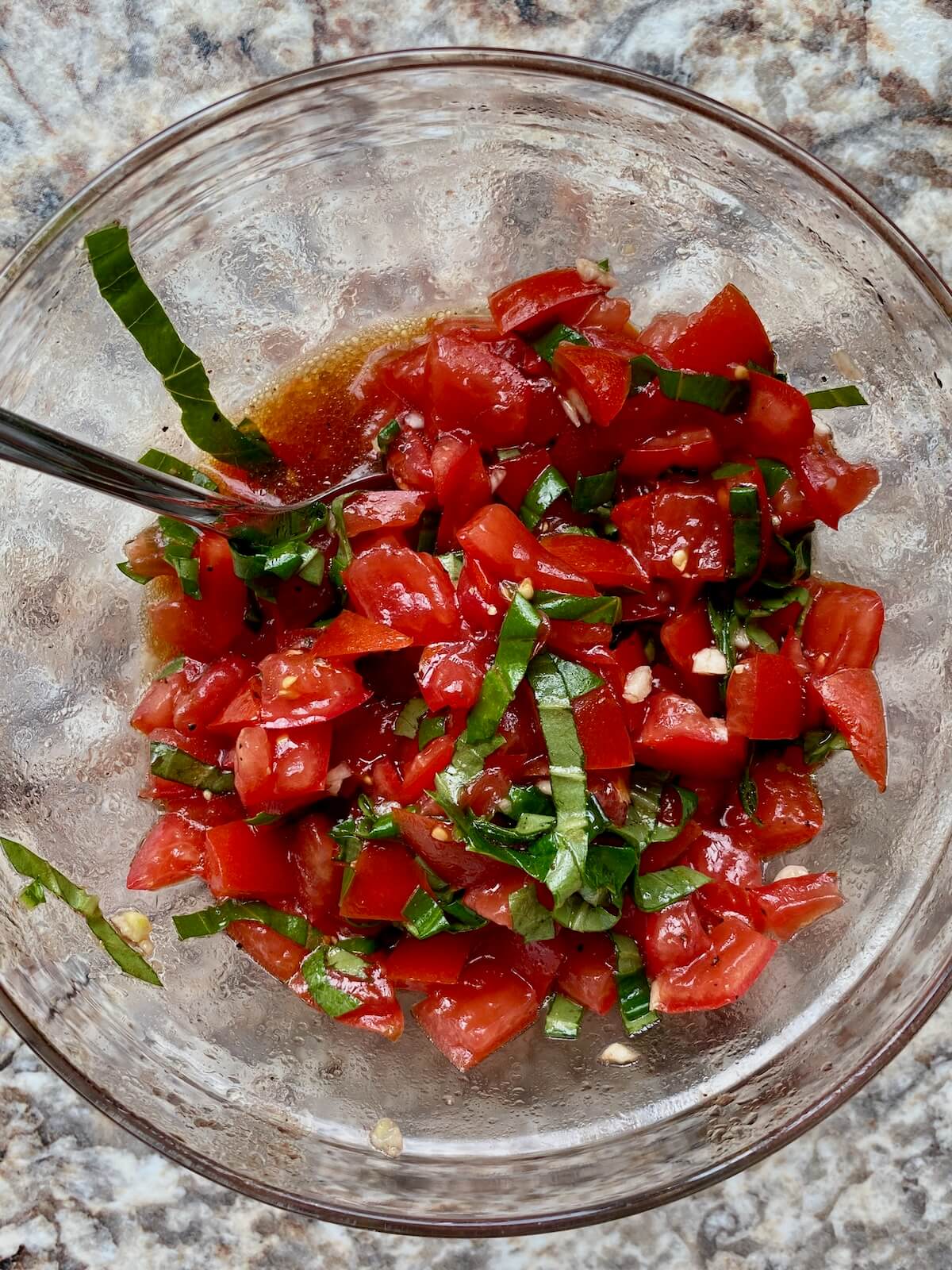 Diced tomatoes, basil, and garlic marinating in a mixture of olive oil and balsamic vinegar in a glass bowl.