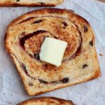 A slice of toasted sourdough cinnamon raisin bread with a pat of butter on top.