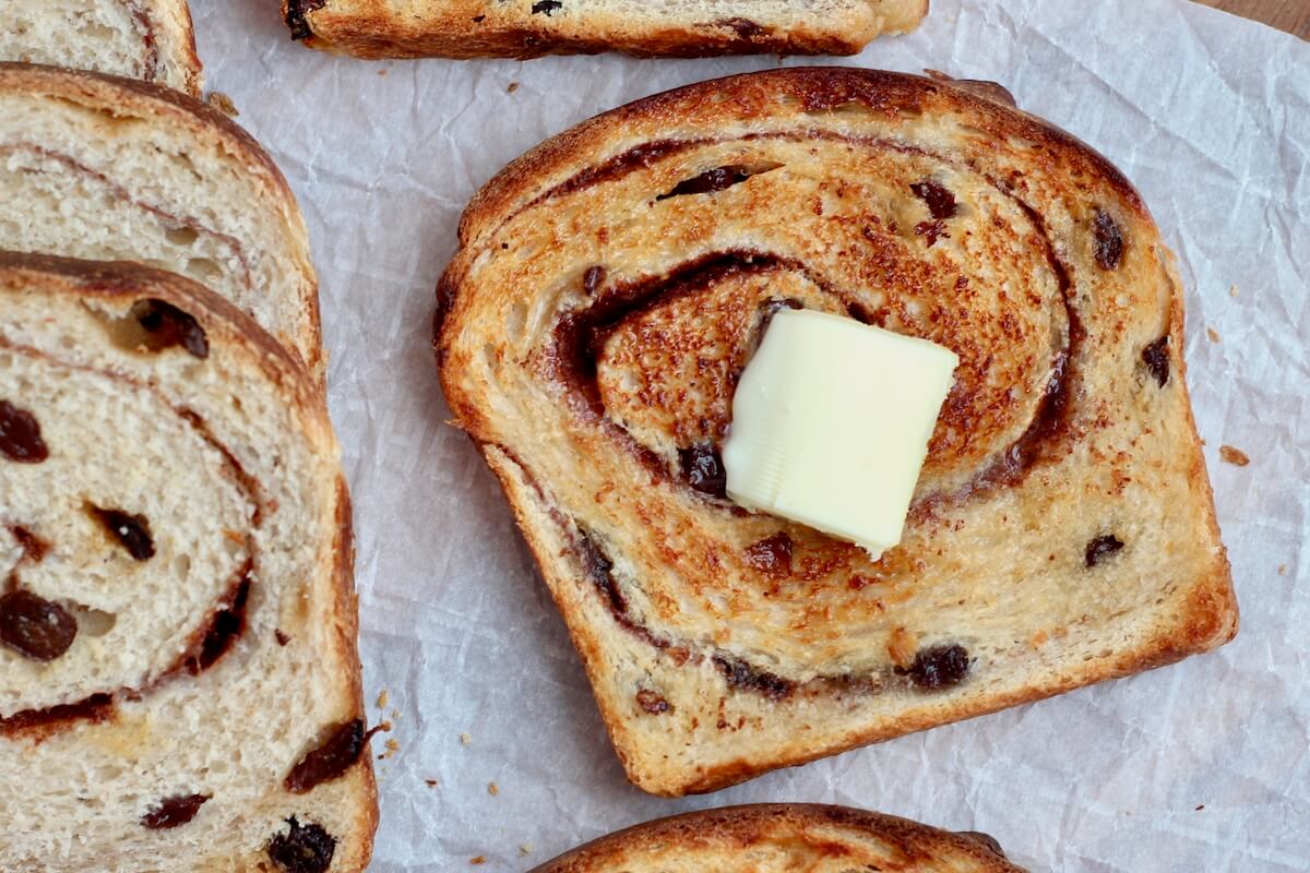 A slice of toasted sourdough cinnamon raisin bread with a pat of butter on top.