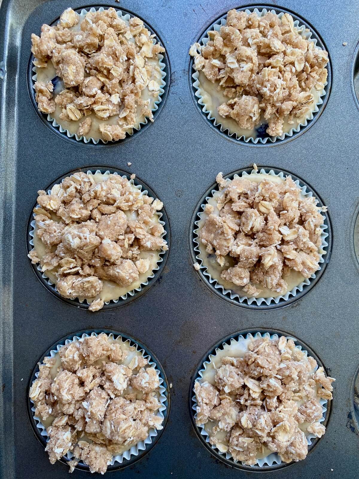 The muffin batter with crumb topping in a paper lined muffin tin.