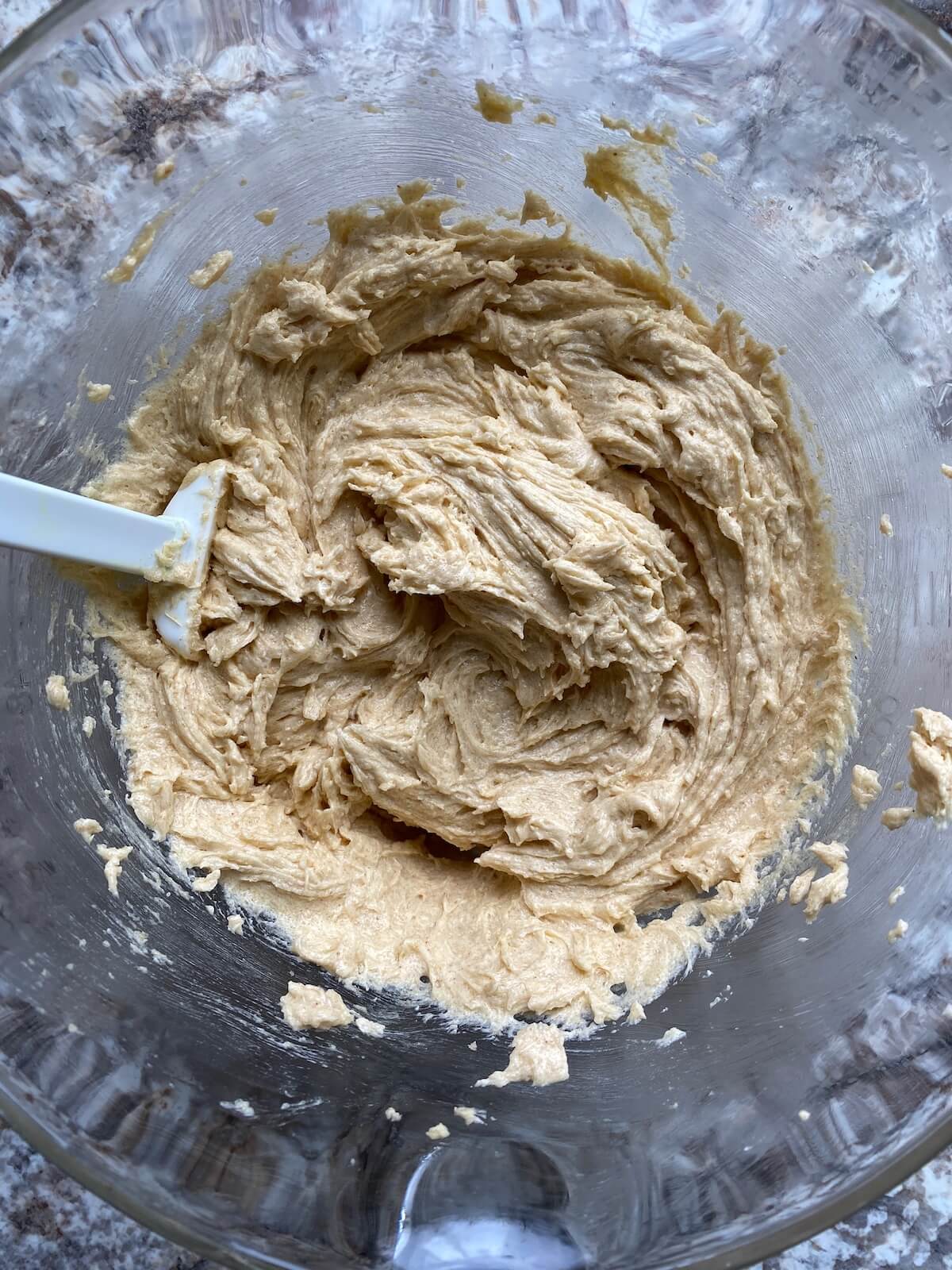 The wet ingredients in a glass mixing bowl with a rubber spatula sticking out to the left.