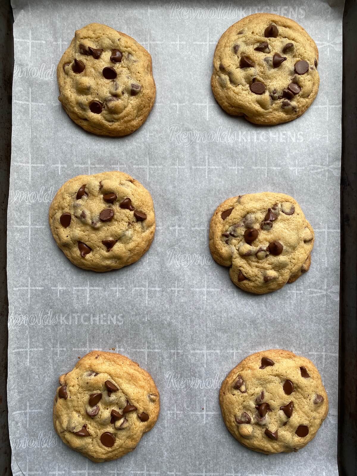 Six baked sourdough chocolate chip cookies on a parchment-lined baking sheet.