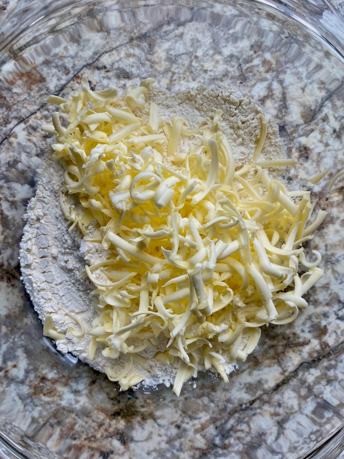 Grated butter added to a mixing bowl with flour.