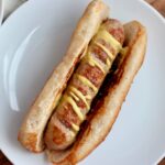 Sausage with mustard in a sourdough hot dog bun on a small plate.