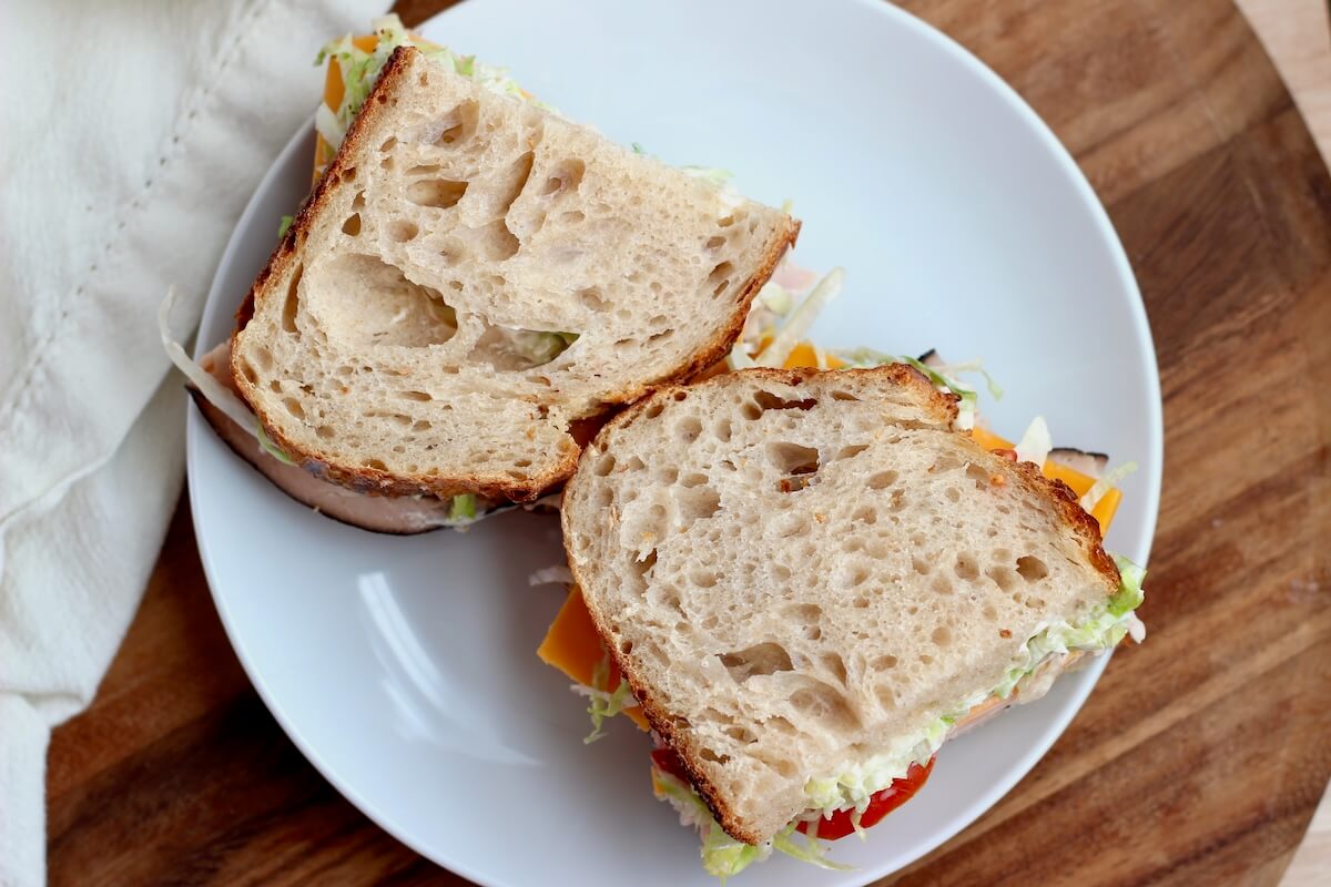 A turkey sandwich on sourdough bread cut in half on a small white plate.