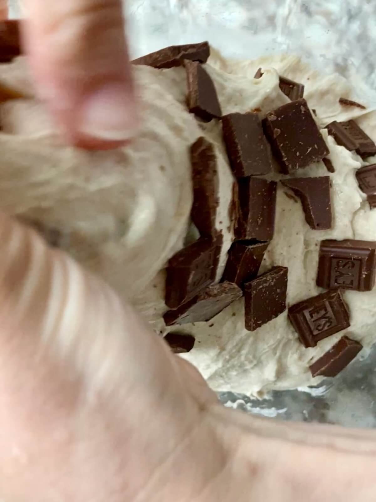 Two hands stretching and folding chocolate pieces into sourdough bread dough.