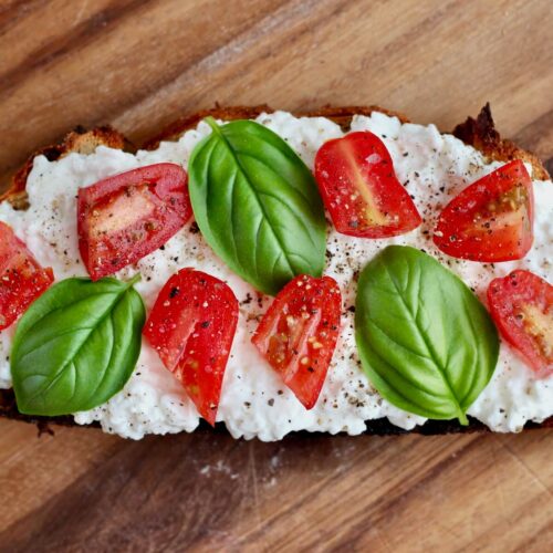 A piece of sourdough cottage cheese toast topped with tomatoes, basil, salt, and pepper.