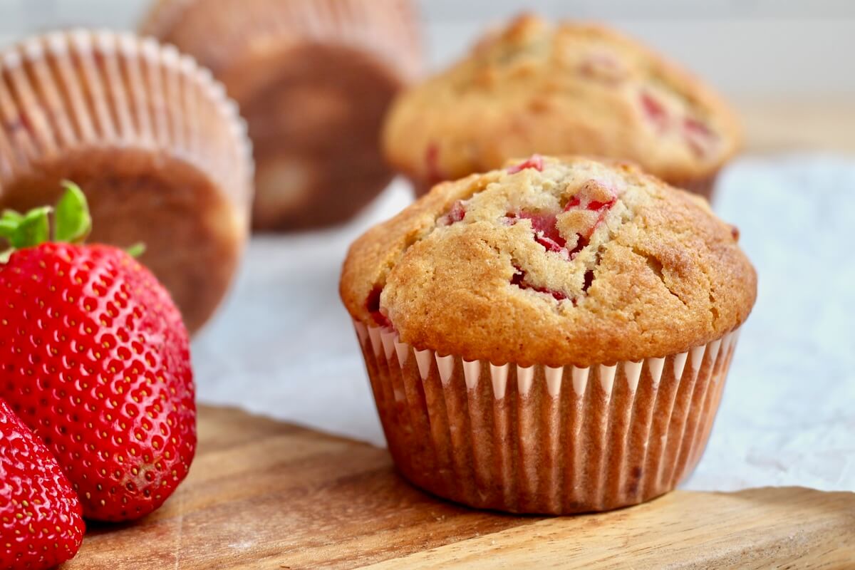 Sourdough strawberry muffins on a counter top. There are fresh strawberries to the left of one of the muffins.