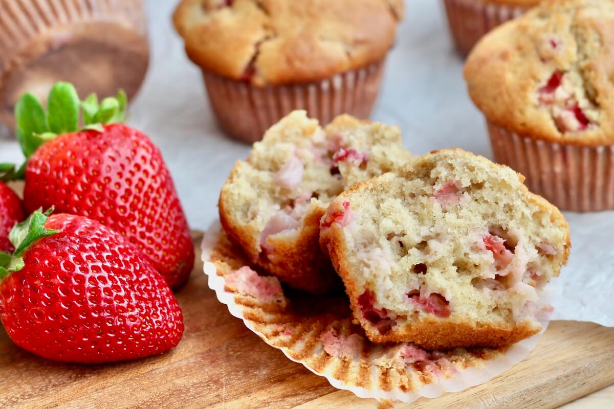 A sourdough strawberry muffin split in half on a paper liner. There are more muffins out of focus in the background.