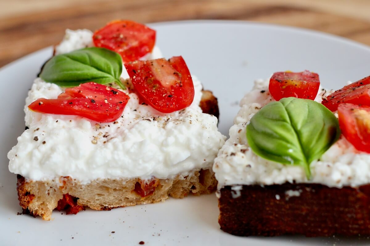 A piece of sun dried tomato sourdough bread topped with cottage cheese, fresh tomatoes, and basil.