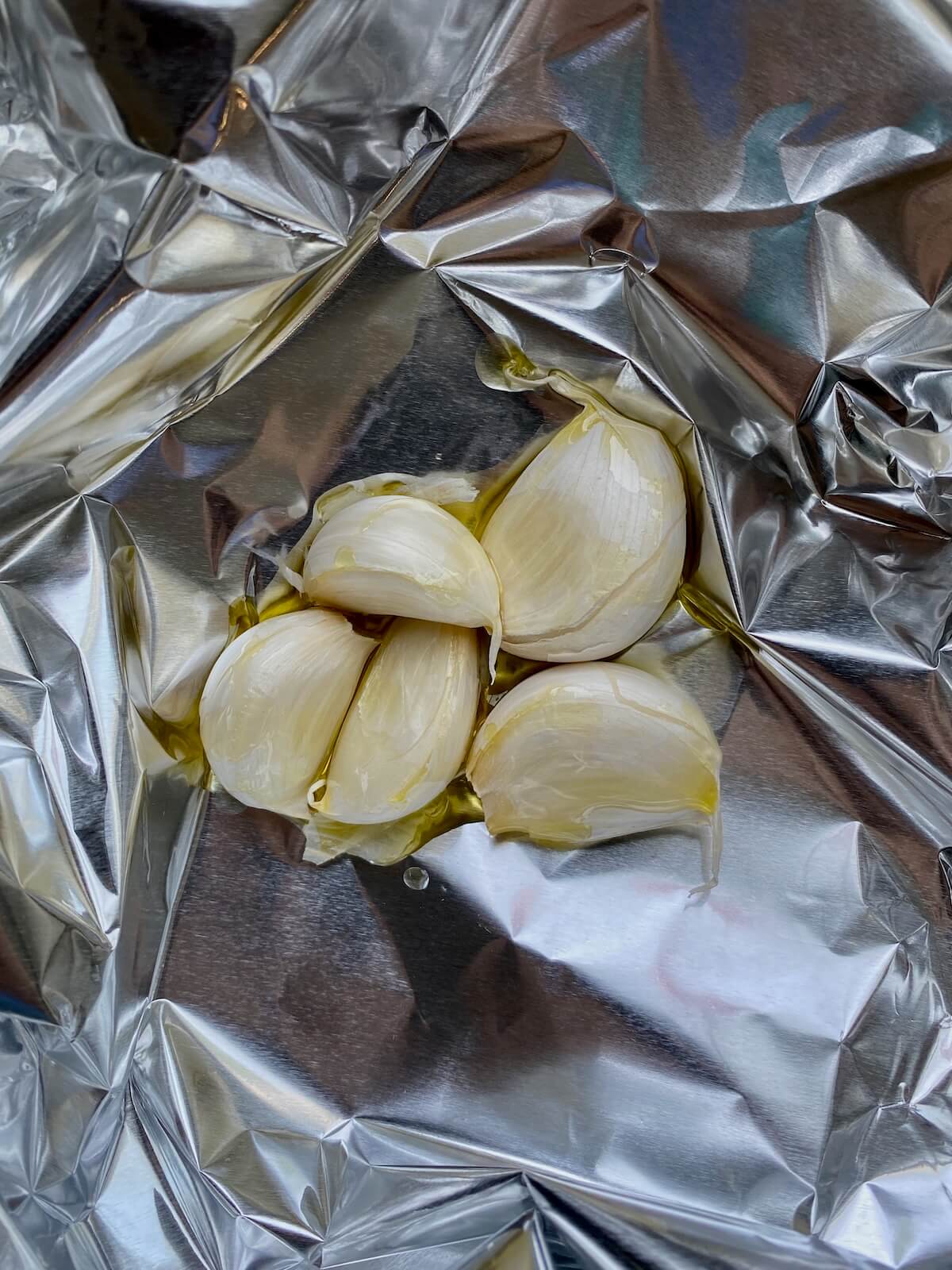 Five cloves of garlic tossed with oil on a piece of aluminum foil.