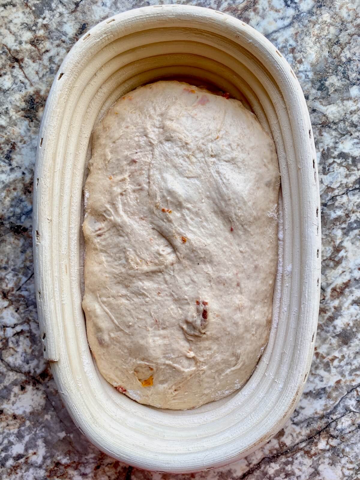 Sun dried tomato sourdough bread dough proofing in an oval-shaped basket.