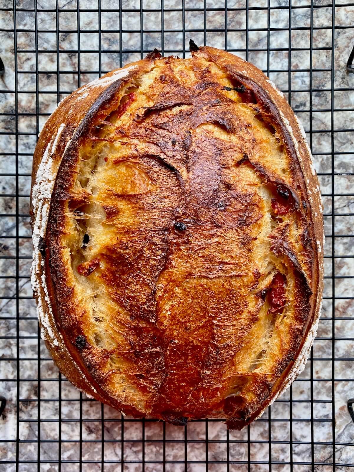 A baked loaf of sun dried tomato sourdough bread on a wire cooling rack.